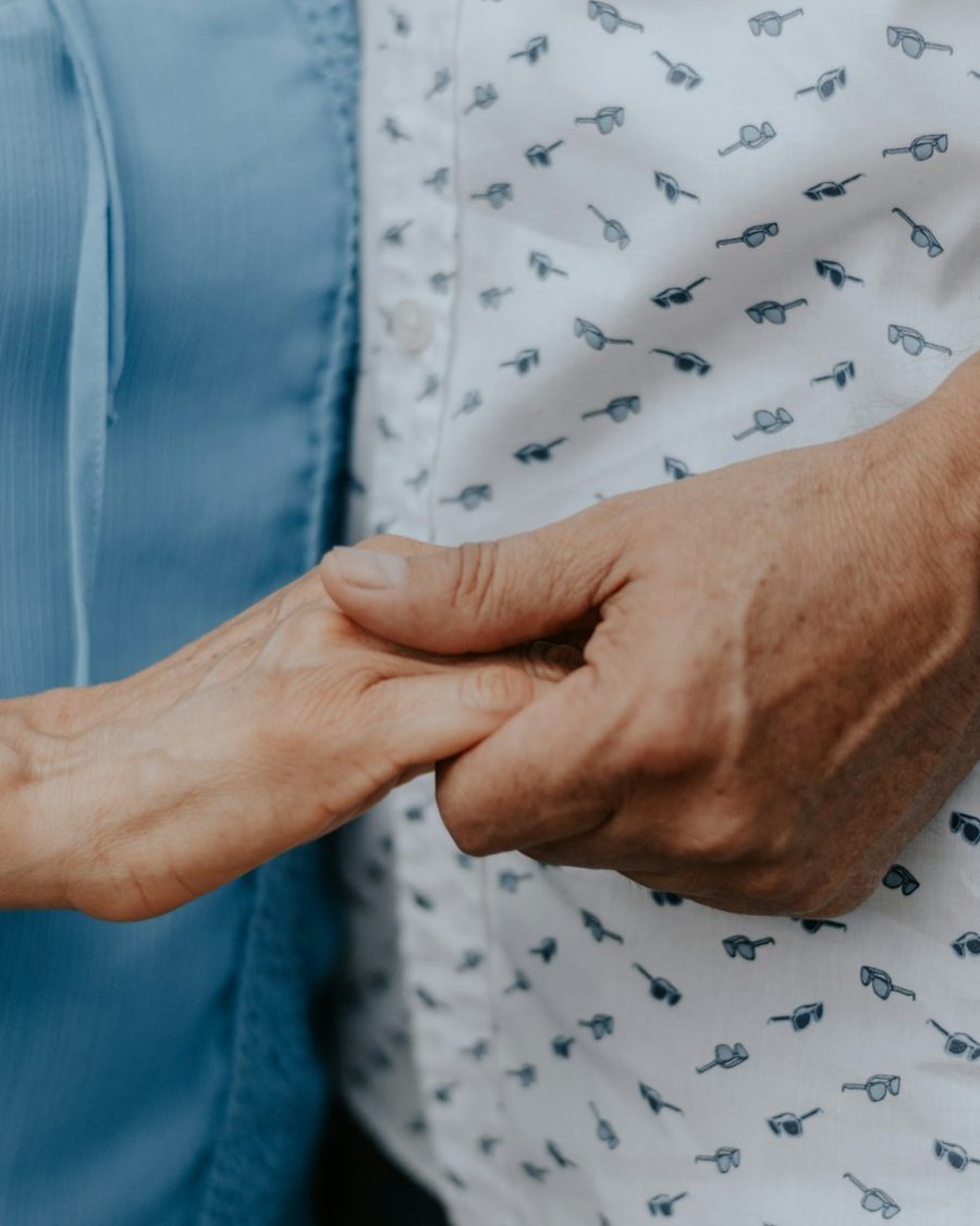 Eine ältere Hand hält eine andere Hand, beide Menschen in hellen Hemden