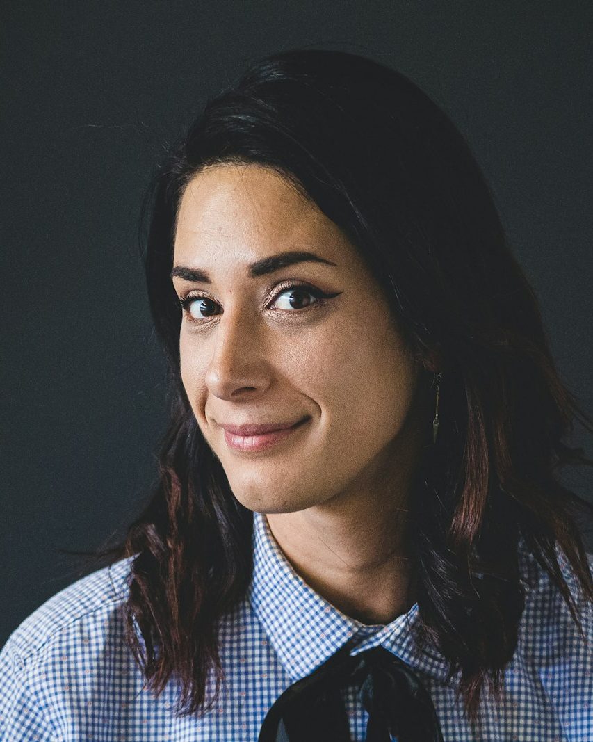 Moderne Website für Coaches, Beispielansicht: Portrait von Miriam Vogt mit schulterlangen dunklen Haaren und kariertem Hemd vor dunkelgrauer Wand, leichtes Lächeln