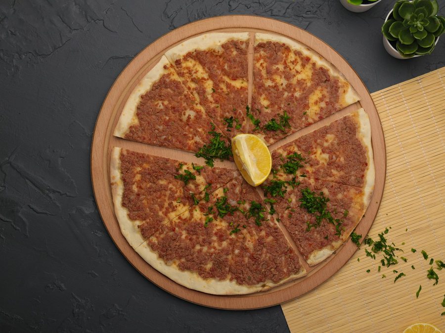 Lahmacun in Stücke geschnitten auf einem Holzbrett, mit Petersilie und einer Zitronenscheibe