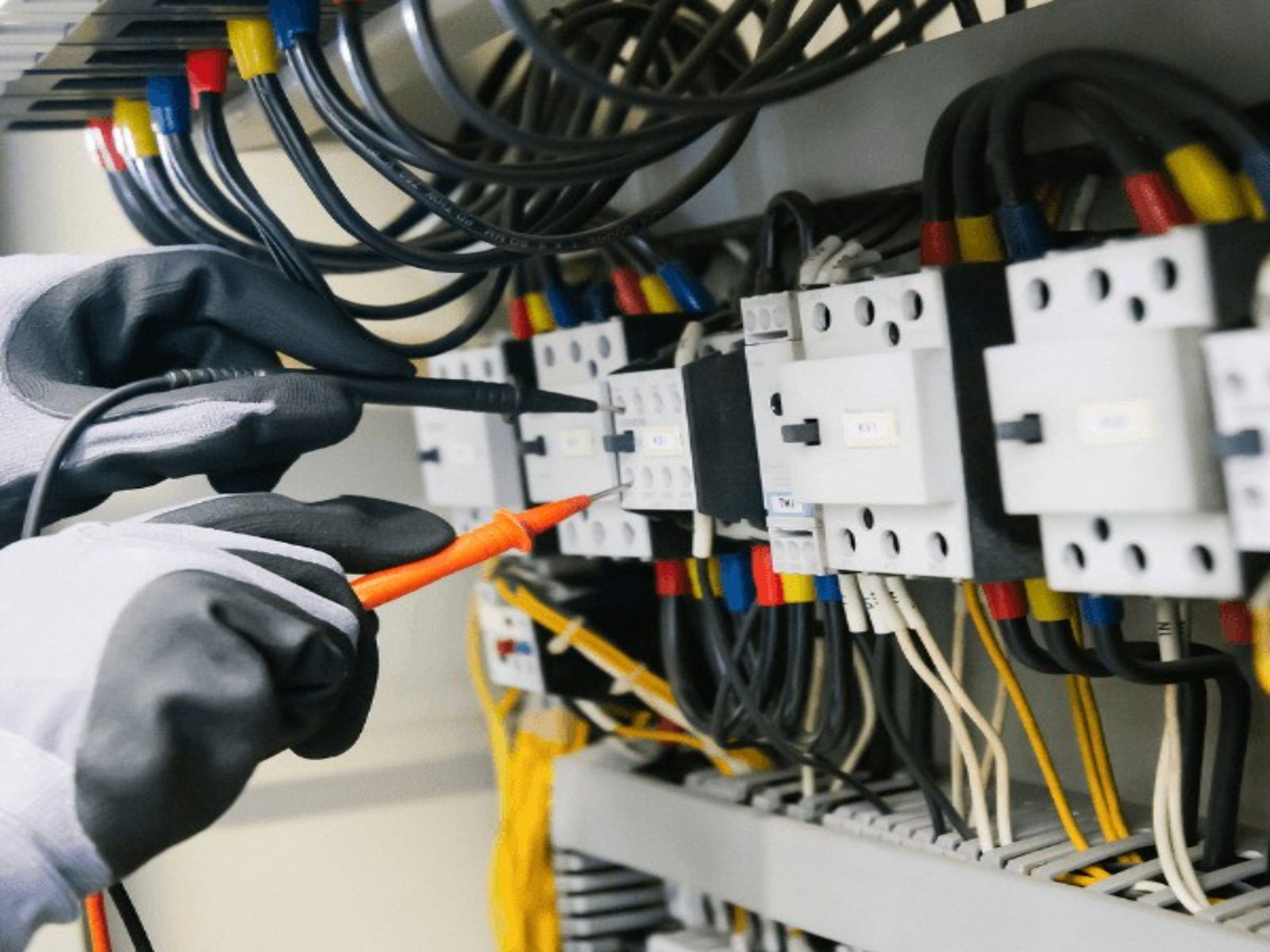 Moderne Website für einen Elektrobetrieb, Beispielansicht: Elektriker mit Arbeitshandschuhen prüft Klemmen im Schaltschrank mit dem Messgerät