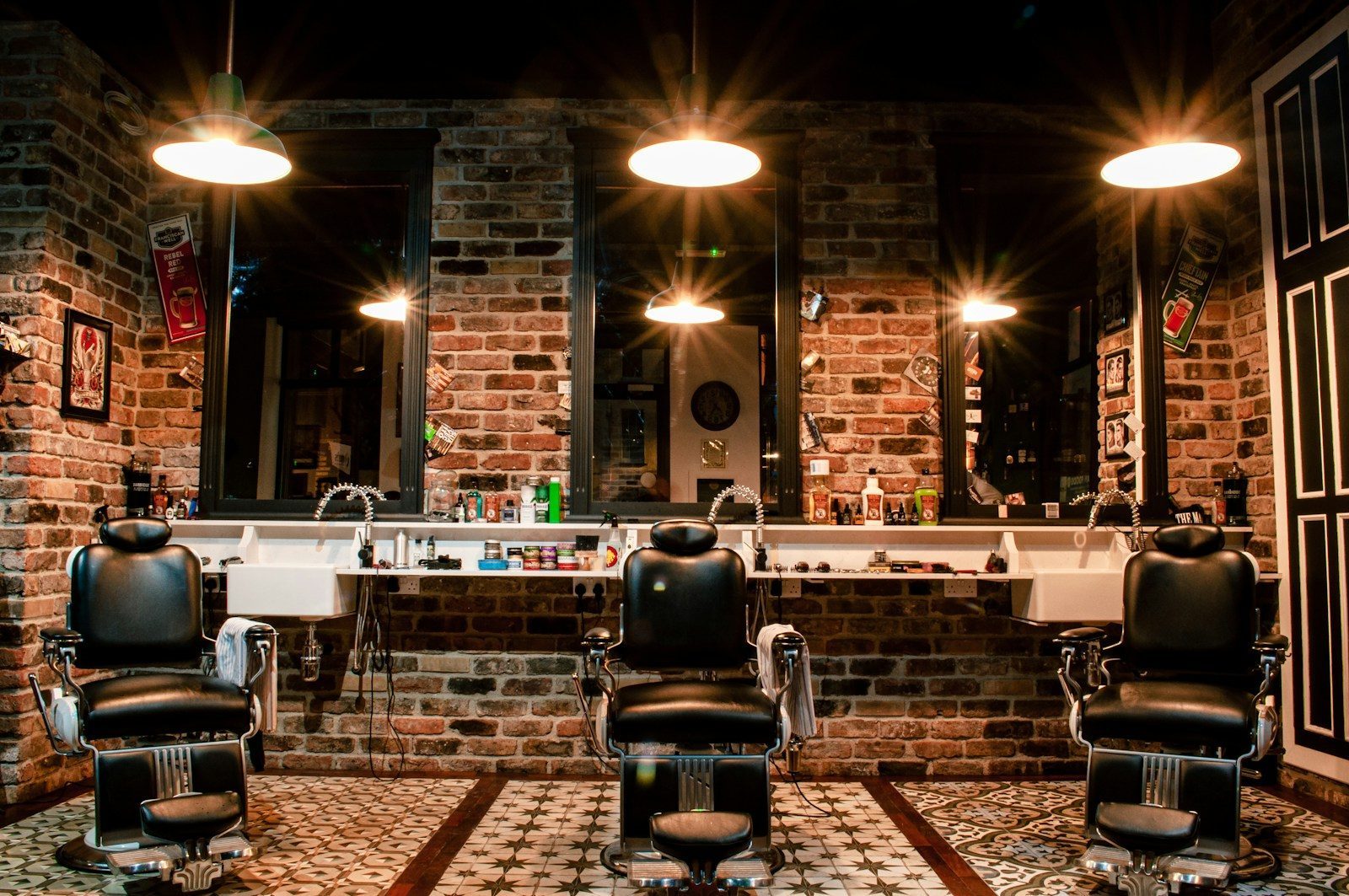 Moderne Website für einen Friseursalon, Beispielansicht: Barbershop mit drei schwarzen Lederstühlen vor Ziegelwand, Spiegeln und warmen Hängelampen