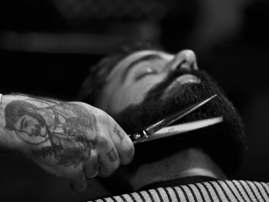 Barber mit tätowierter Hand stutzt einen Vollbart mit der Schere, schwarz-weiß