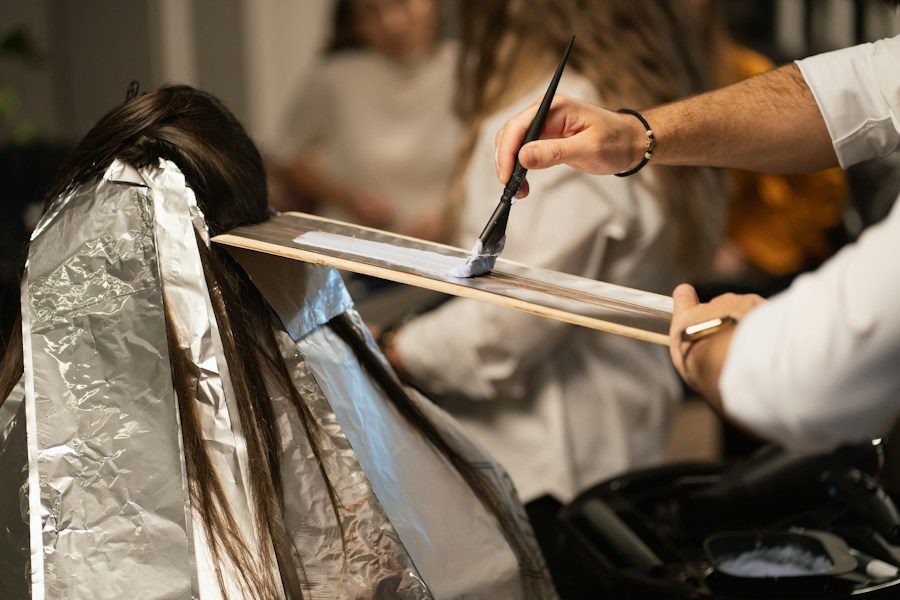 Coloristin im Friseursalon trägt Farbe mit dem Pinsel auf eine Haarsträhne auf, daneben Folien für die Balayage