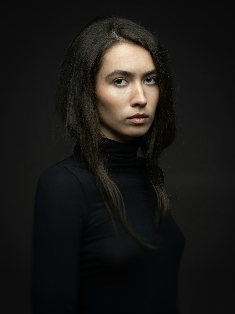 Portrait von Lena, Inhaberin, mit langen dunklen Haaren vor dunklem Hintergrund