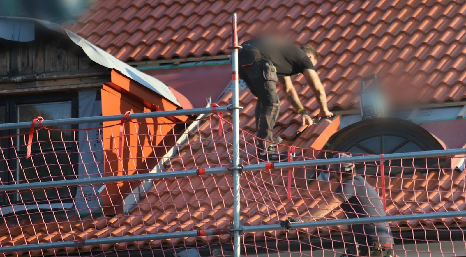 Moderne Website für einen Handwerksbetrieb, Beispielansicht: Dachdecker arbeitet auf einem roten Ziegeldach über einer Gaube, davor ein Gerüst mit Schutznetz