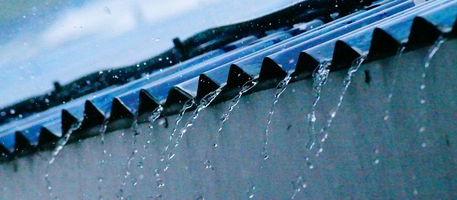 Regenwasser läuft in Strahlen von der Kante eines Wellblechdachs