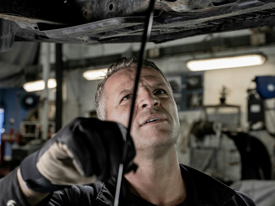 Mechaniker steht unter einem Auto auf der Hebebühne und prüft mit einer Lampe den Unterboden