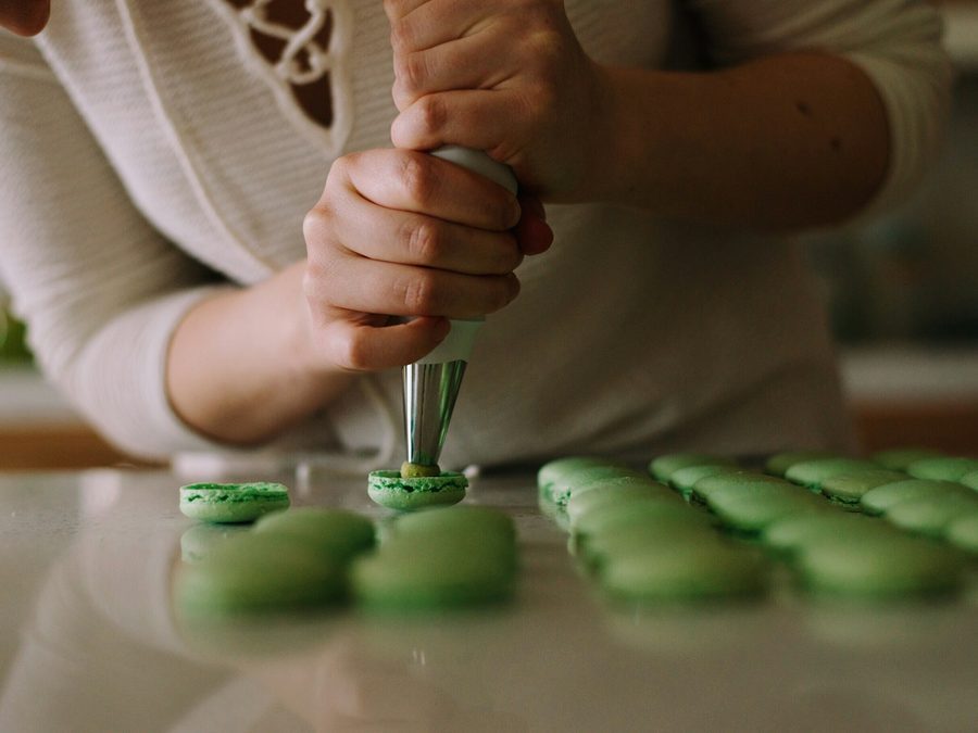 Konditorin spritzt mit dem Spritzbeutel grüne Macaron-Schalen auf eine helle Arbeitsplatte