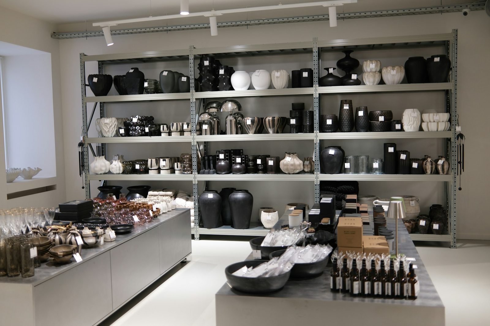 Moderne Website für einen Laden, Beispielansicht: heller Laden mit Metallregal voller Vasen in Schwarz und Weiß, davor zwei Tische mit Gläsern, Schalen und Kerzen