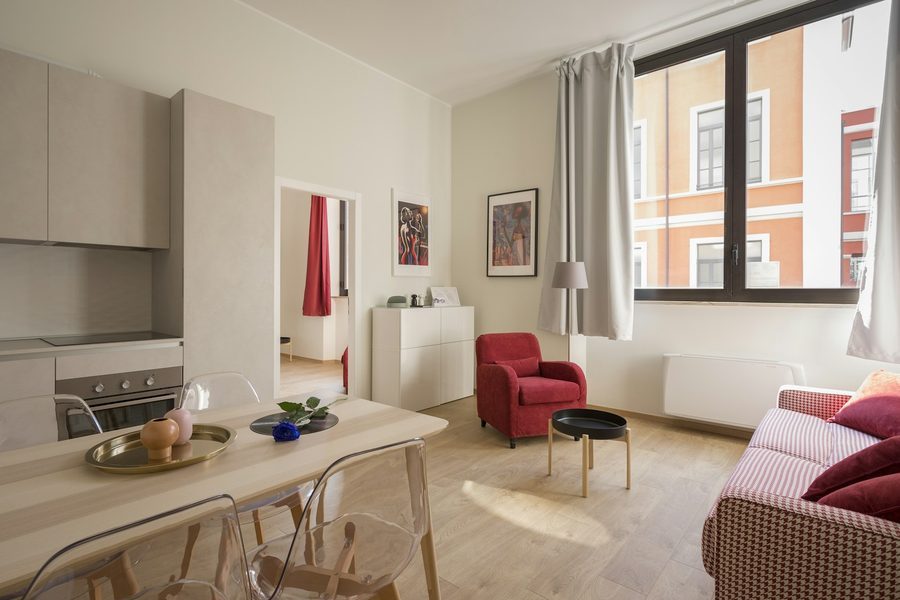 Helles Wohnzimmer mit offener Küche, Esstisch mit transparenten Stühlen, rotem Sessel und großem Fenster zur Straße