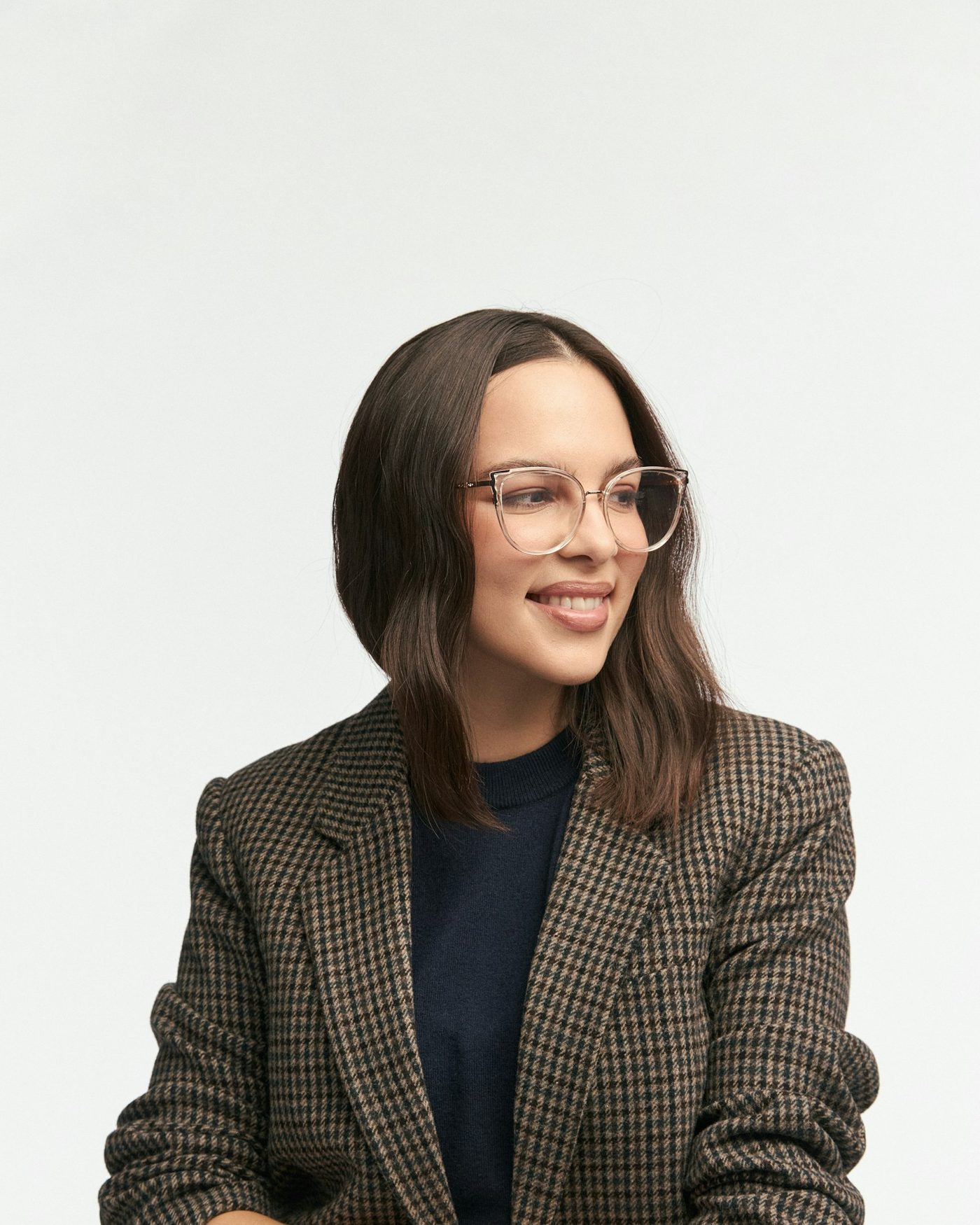Moderne Website für einen Optiker, Beispielansicht: Frau mit transparenter Brille mit feinem Metallrahmen und kariertem Blazer lächelt zur Seite, heller Hintergrund