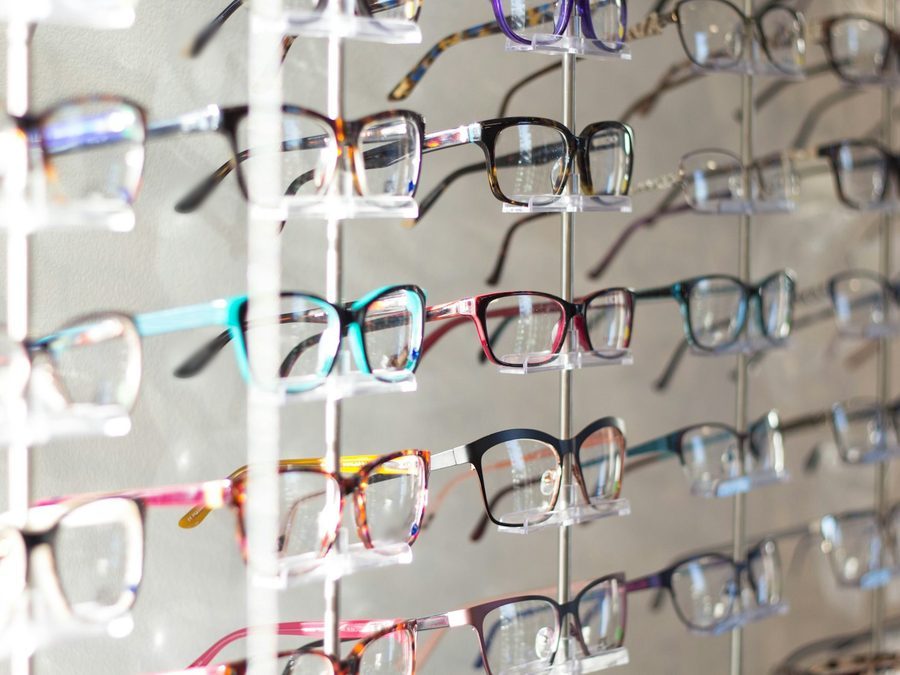 Brillenwand im Optikergeschäft mit Fassungen in Schwarz, Havanna, Türkis und Rot auf durchsichtigen Haltern