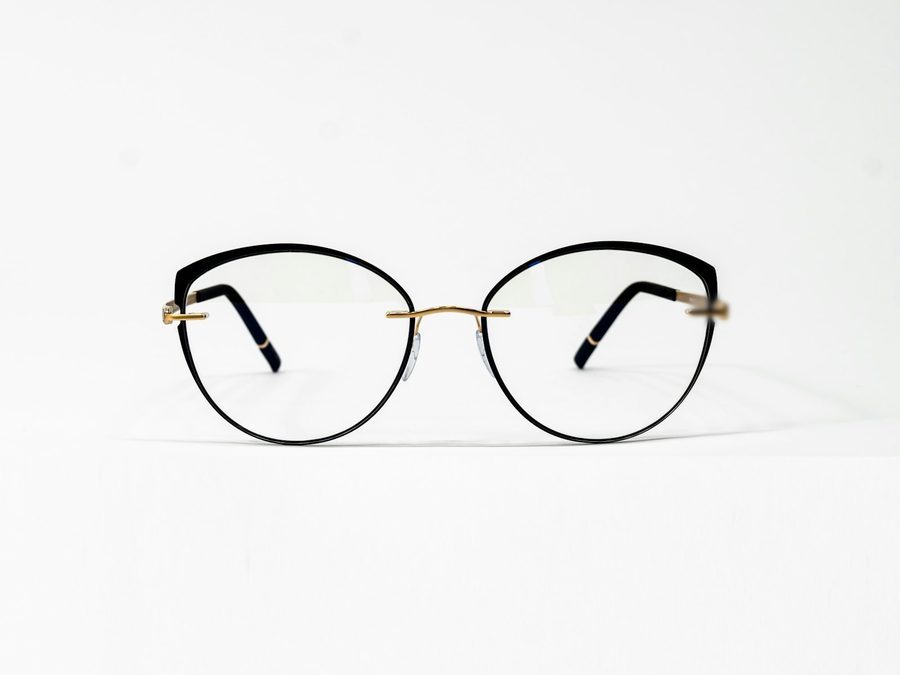 Schwarze Brille mit goldenem Steg, frontal auf weißem Grund