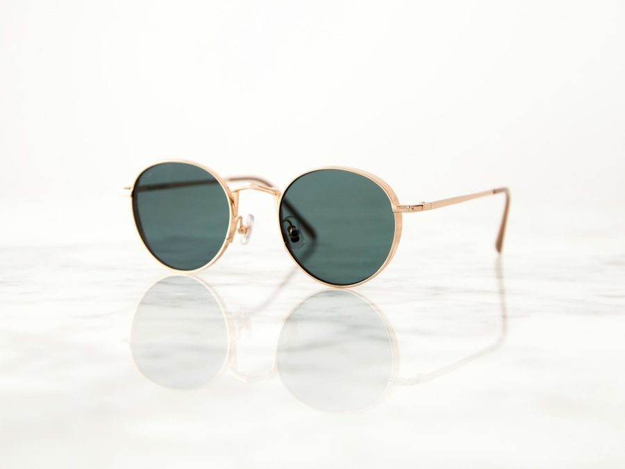 Runde Sonnenbrille mit goldenem Metallrahmen und grünen Gläsern auf weißem Marmor