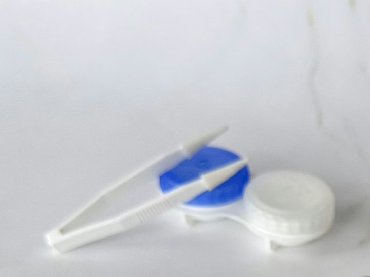Blau-weißer Kontaktlinsenbehälter mit Pinzette auf hellem Marmor