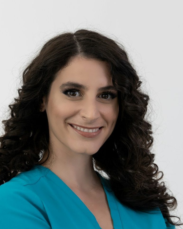 Portrait von Sarah Nowak, Physiotherapeutin, mit langen dunklen Locken und petrolfarbener Praxiskleidung