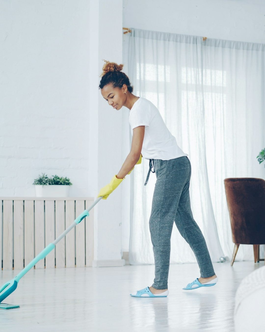 Moderne Website für eine Reinigungsfirma, Beispielansicht: Reinigungskraft im weißen T-Shirt mit gelben Handschuhen wischt mit einem türkisen Flachmopp den hellen Boden einer Wohnung