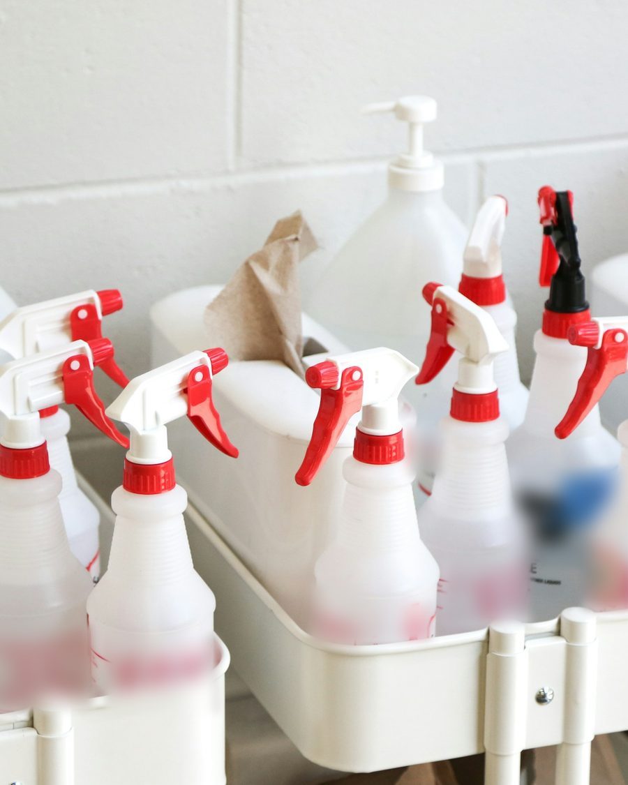 Weißer Reinigungswagen mit Sprühflaschen, Pumpflaschen und Papiertüchern vor einer hellen Wand