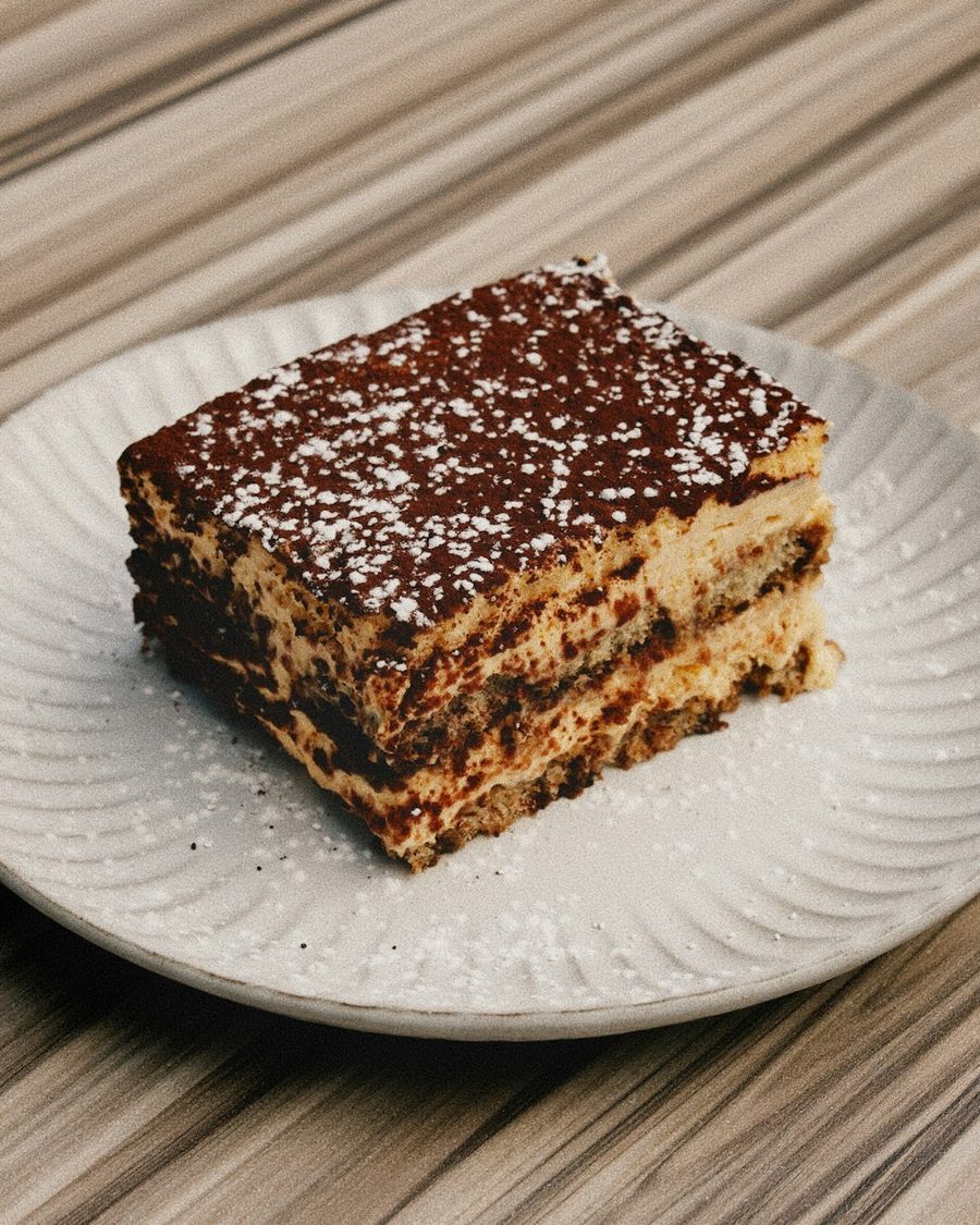 Stück Tiramisu mit Kakao auf einem hellen Teller auf Holz