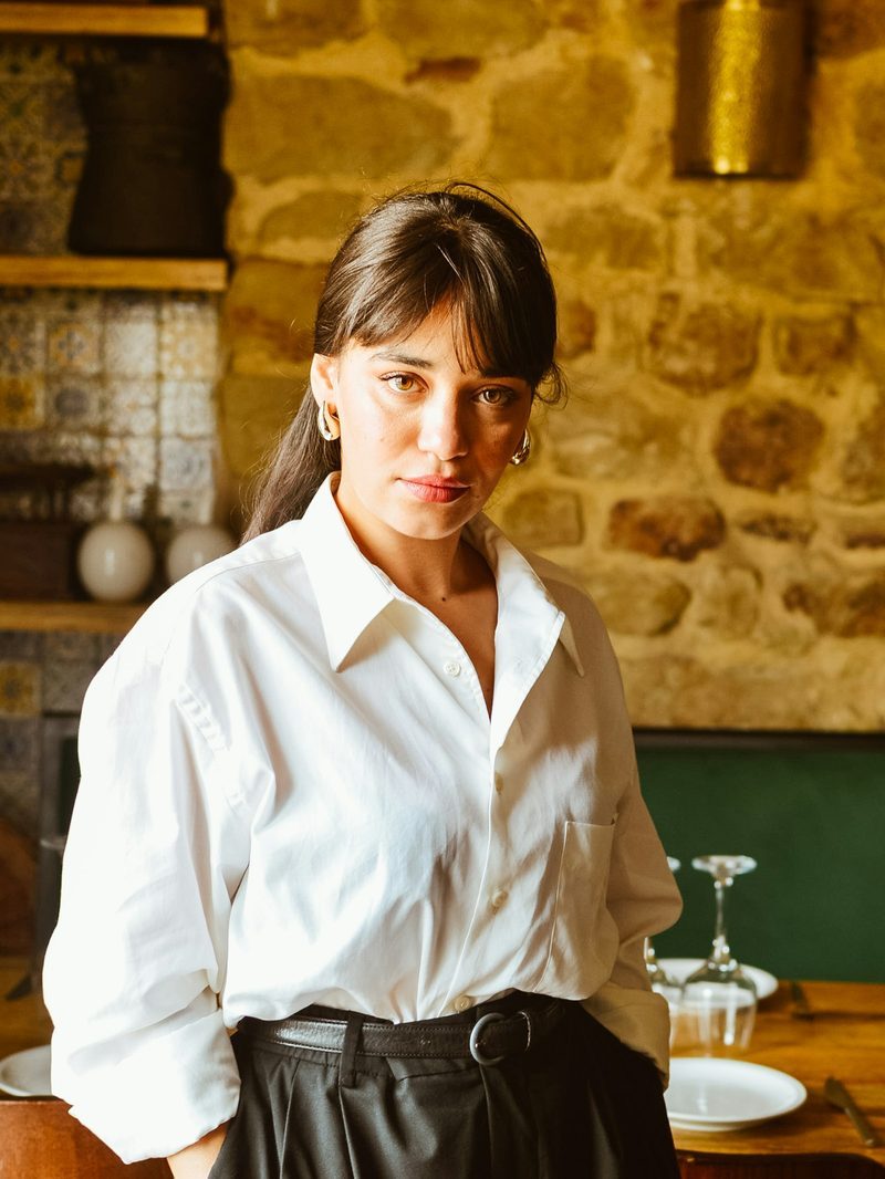 Portrait von Giulia, Service, mit weißer Bluse vor einer Steinwand im Gastraum