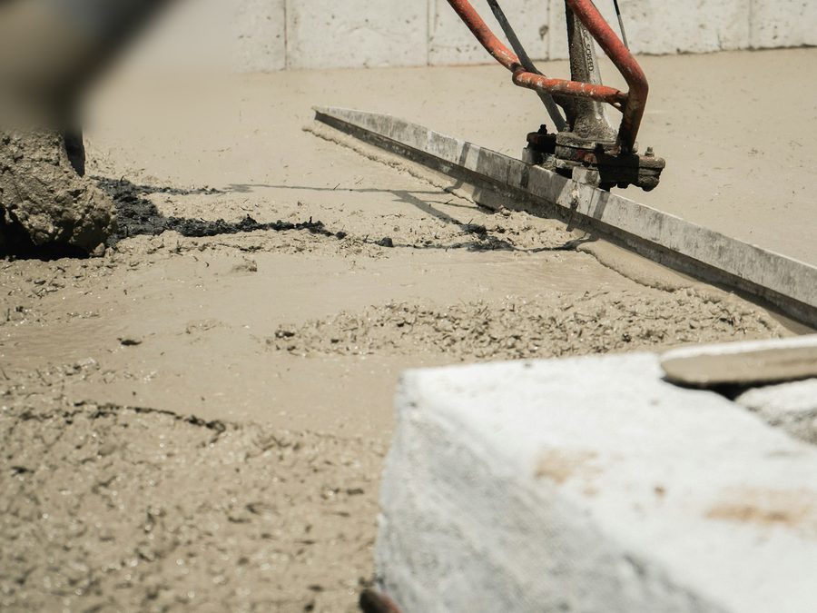 Frischer Zementestrich wird mit einer Rüttelbohle glatt abgezogen