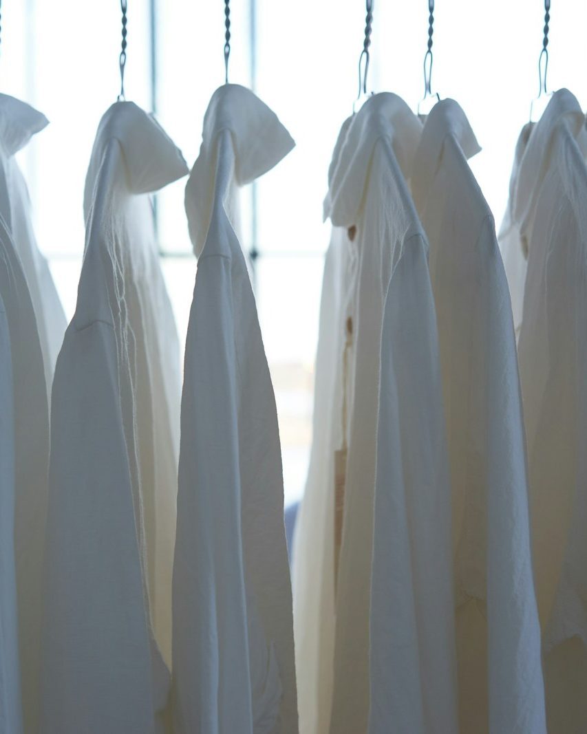 Frisch gereinigte weiße Hemden hängen auf Bügeln vor einem hellen Fenster