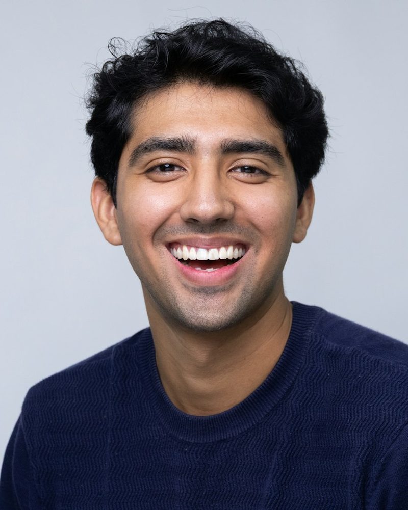 Portrait von Jonas mit dunklen Locken und dunkelblauem Pullover, er lacht in die Kamera